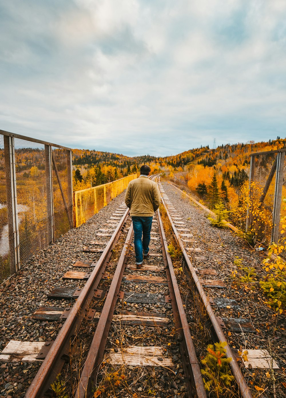 man in green jacket walking on train rail during daytime