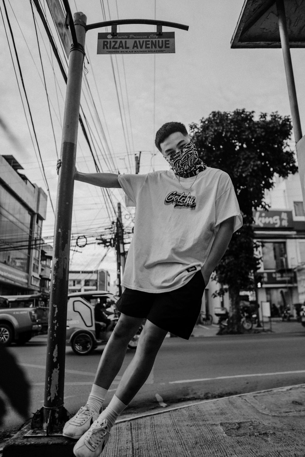 man in white crew neck t-shirt and black shorts standing on street during daytime