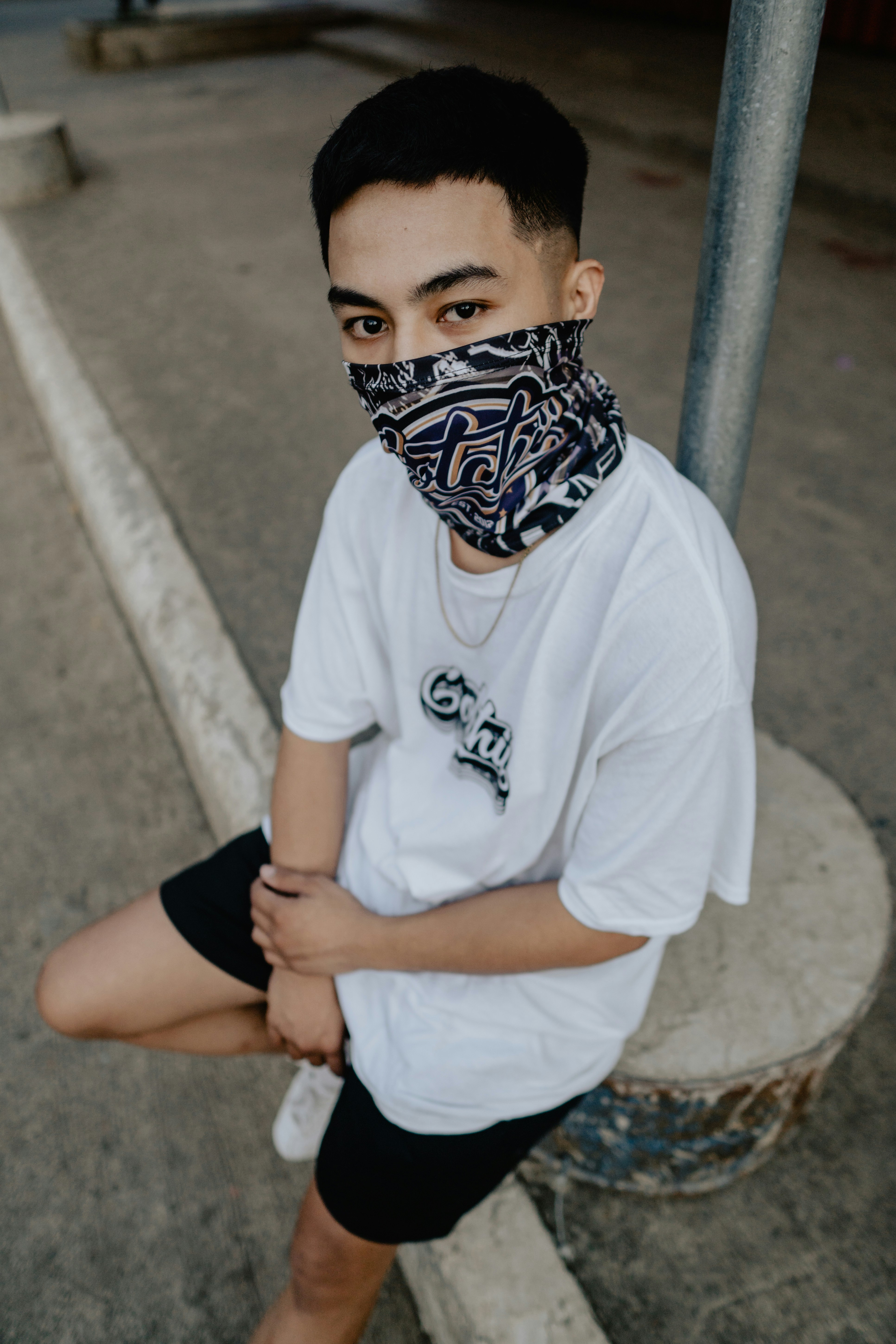 man in white crew neck t-shirt and black shorts sitting on concrete bench during daytime