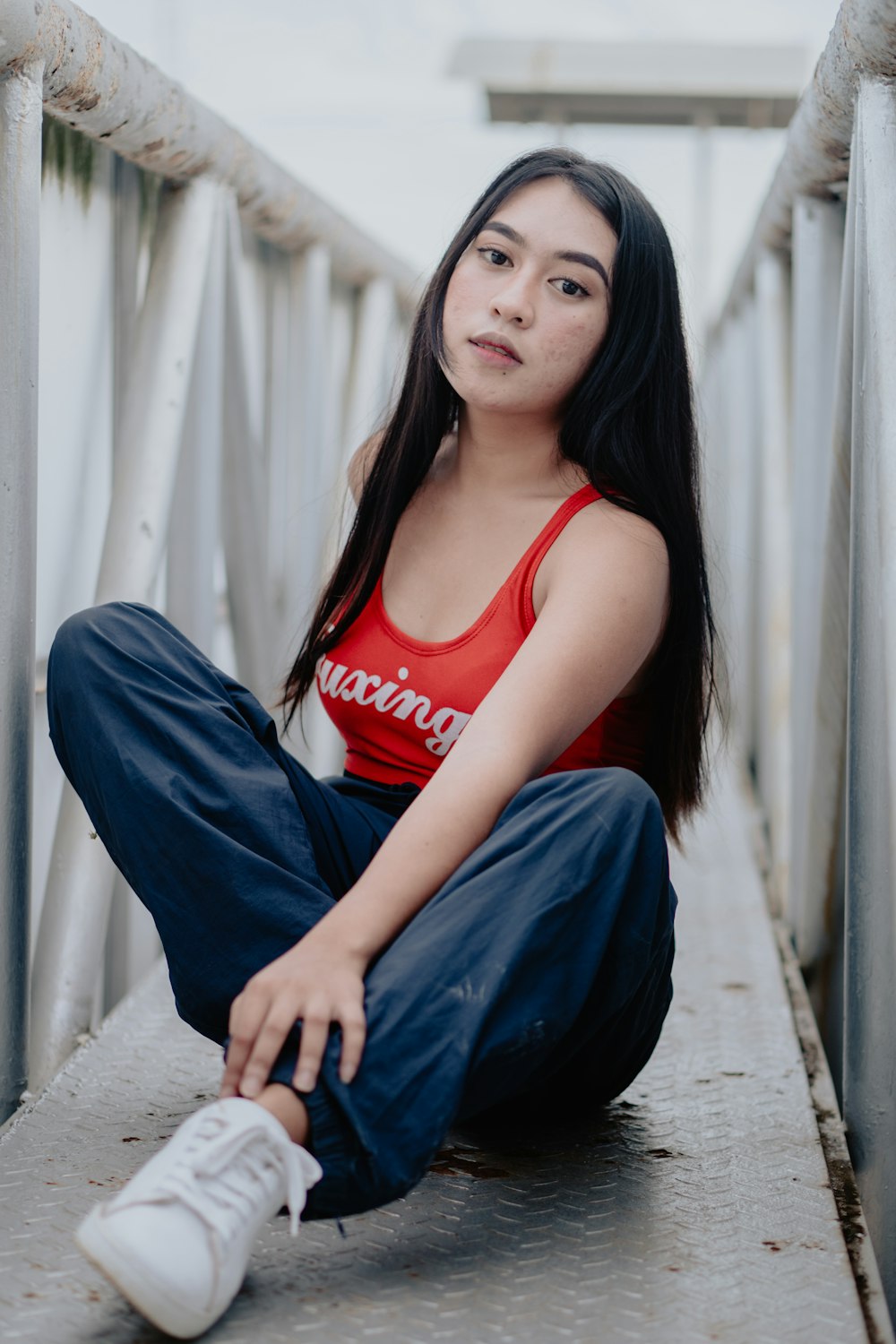 woman in red tank top and blue denim jeans sitting on concrete floor