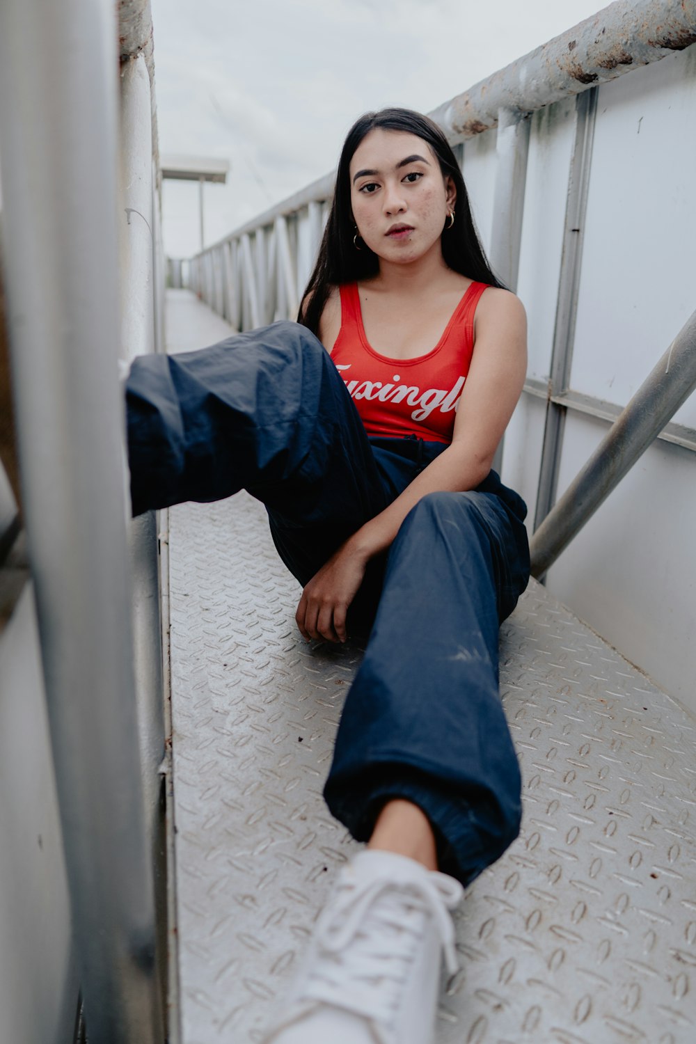 woman in red tank top and blue denim jeans sitting on white concrete wall