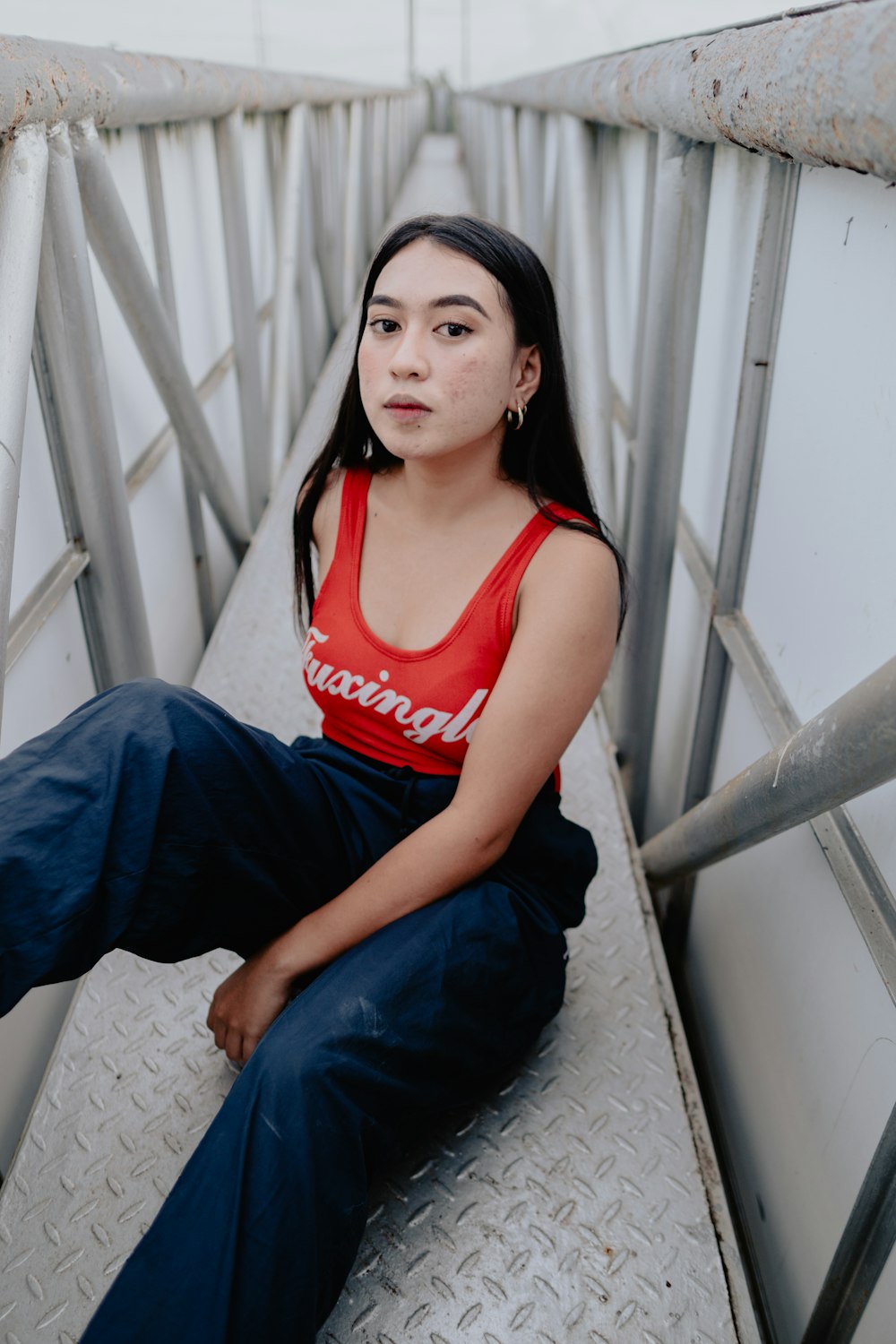 woman in red tank top and blue denim jeans sitting on white concrete wall
