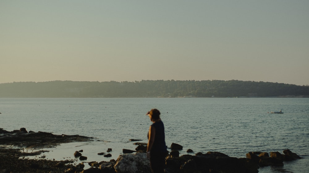 woman in black shirt sitting on rock near body of water during daytime