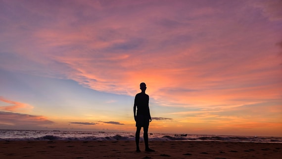 silhouette of man standing on beach during sunset
