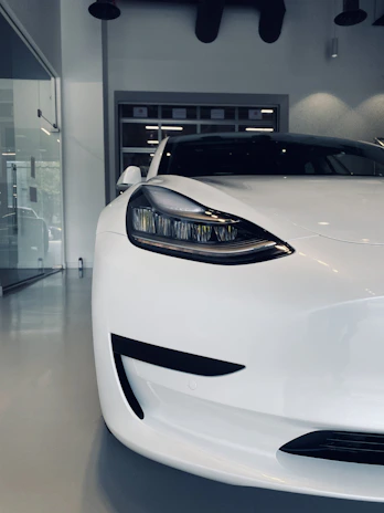 A sleek conventional car parked with a glowing crimson light highlighting its battery compartment.