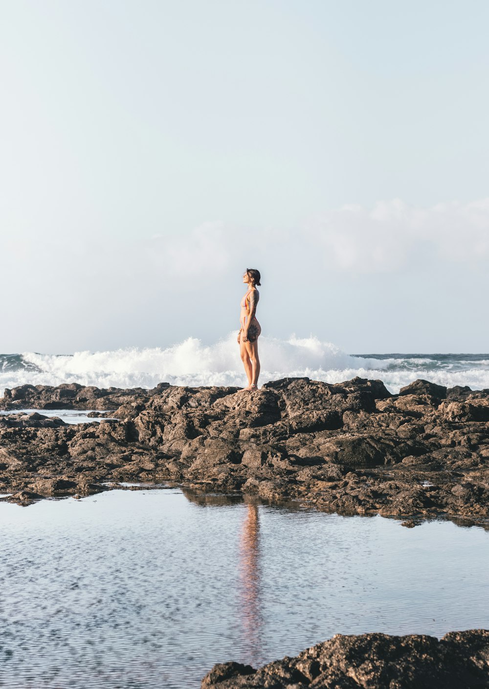 mulher no biquíni preto em pé na formação rochosa perto do corpo de água durante o dia
