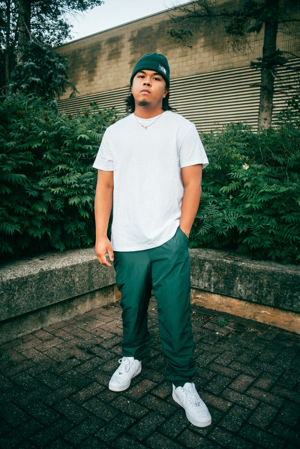 man in white crew neck t-shirt and black pants standing near green plants during daytime