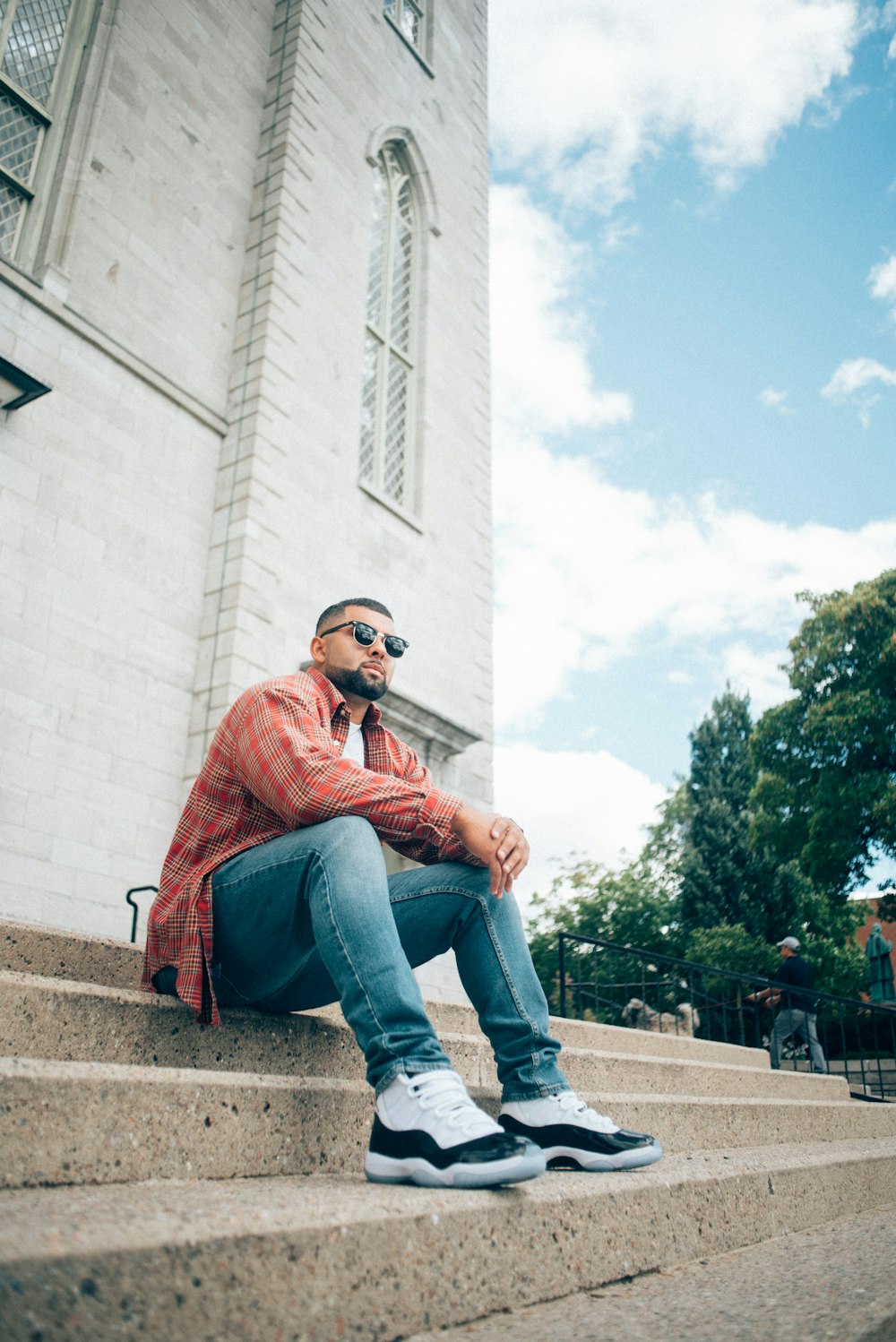 man in red dress shirt and blue denim jeans sitting on brown concrete bench during daytime