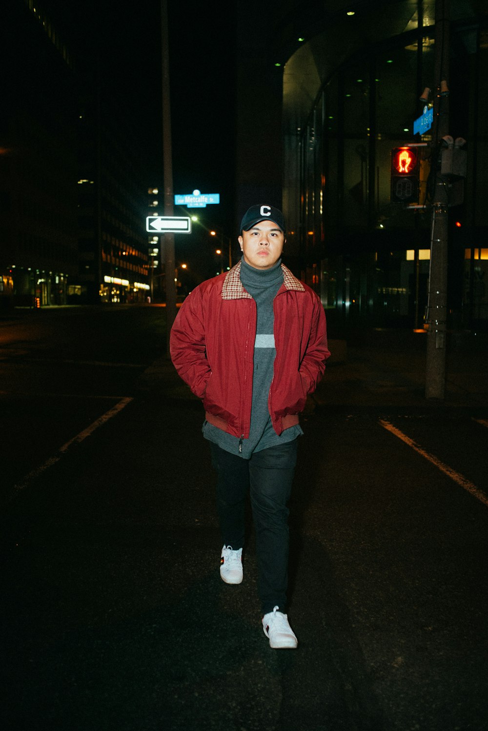 man in red jacket standing on sidewalk during night time