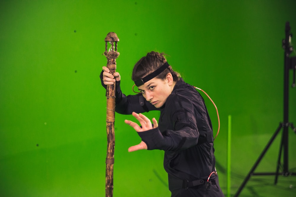 man in black jacket holding brown wooden stick