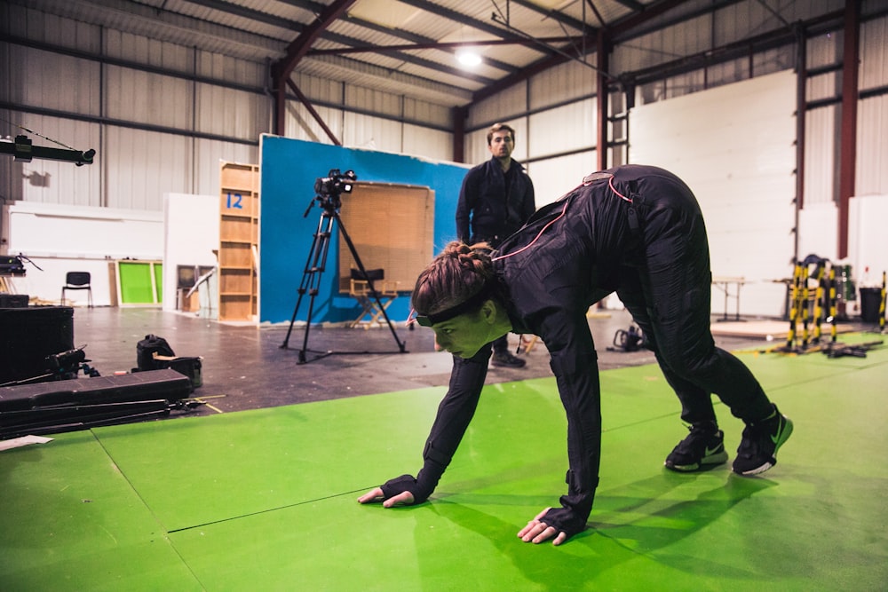 man in black leather jacket and black pants kneeling on green floor