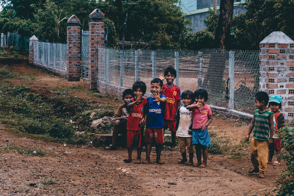 group of children sitting on ground near gray metal fence during daytime