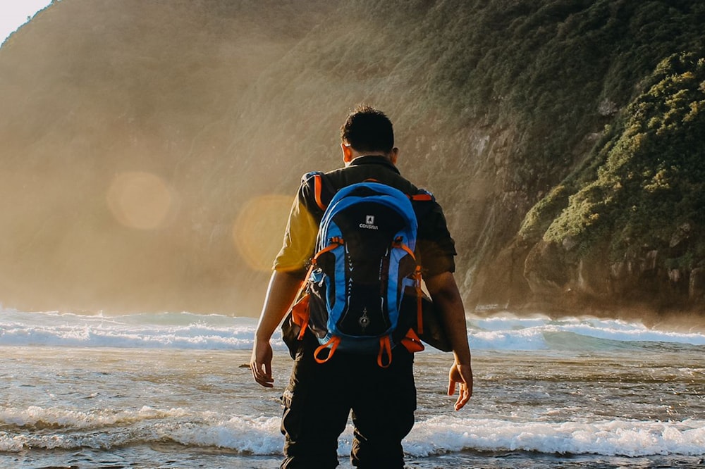 man in black and red backpack walking on seashore during daytime