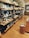 A well-organized retail display featuring various kitchenware items such as plates, bowls, and cups. The shelves are neatly arranged along a wall, showcasing different sizes and styles of dishware. The setting has a warm, inviting atmosphere with wooden floors and soft lighting.