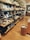 A well-organized retail display featuring various kitchenware items such as plates, bowls, and cups. The shelves are neatly arranged along a wall, showcasing different sizes and styles of dishware. The setting has a warm, inviting atmosphere with wooden floors and soft lighting.