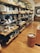 A well-organized retail display featuring various kitchenware items such as plates, bowls, and cups. The shelves are neatly arranged along a wall, showcasing different sizes and styles of dishware. The setting has a warm, inviting atmosphere with wooden floors and soft lighting.