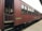 A vintage passenger train car painted in red with wooden paneling and several windows. The train is stationary on tracks next to a platform. The side of the car has a sign that reads 'Blue Bird'. The setting suggests an old-fashioned or historical railway experience.