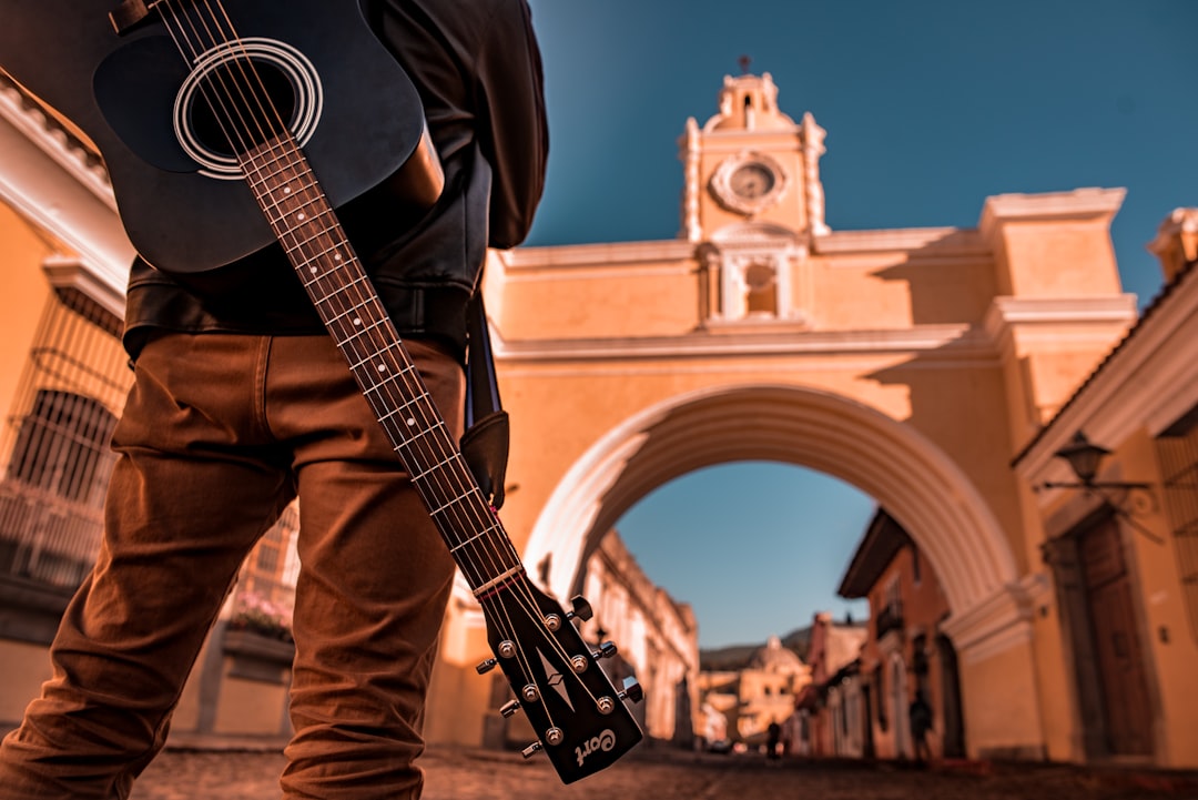 man in brown jacket playing acoustic guitar, Música en la Calle del Arco de la Antigua Guatemala.