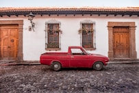 red vintage car parked beside white concrete building during daytime