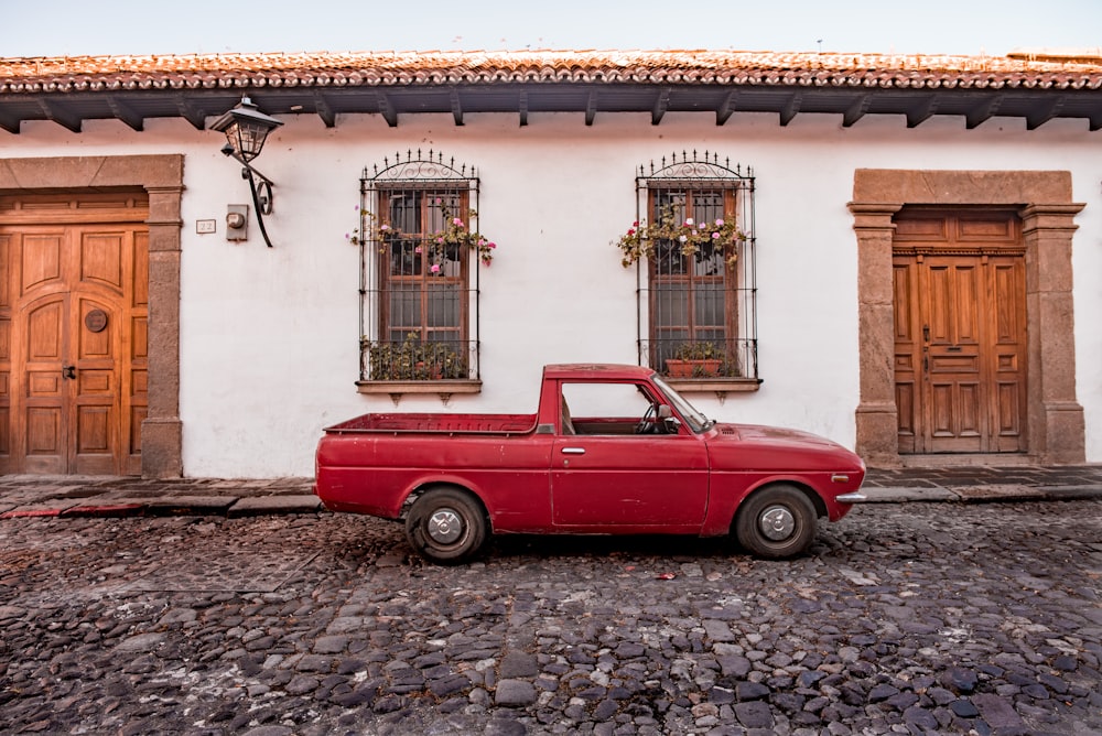 red vintage car parked beside white concrete building during daytime