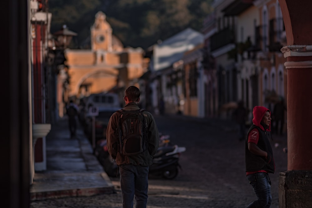 man in black and red jacket standing on road during daytime