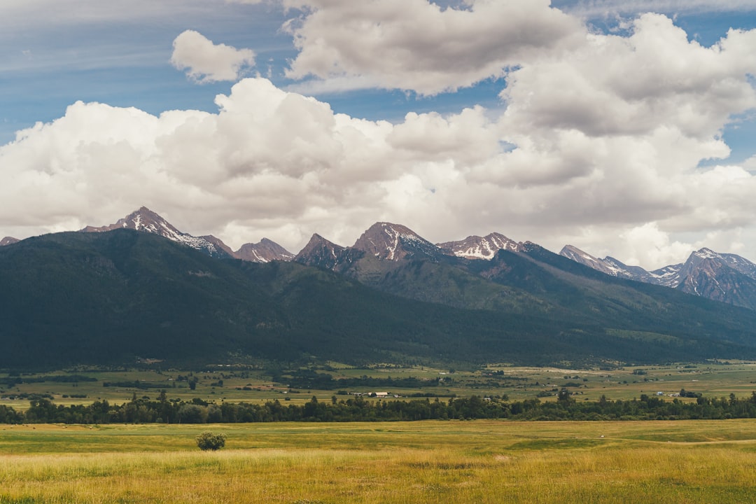 green grass field near mountain under white clouds during daytime