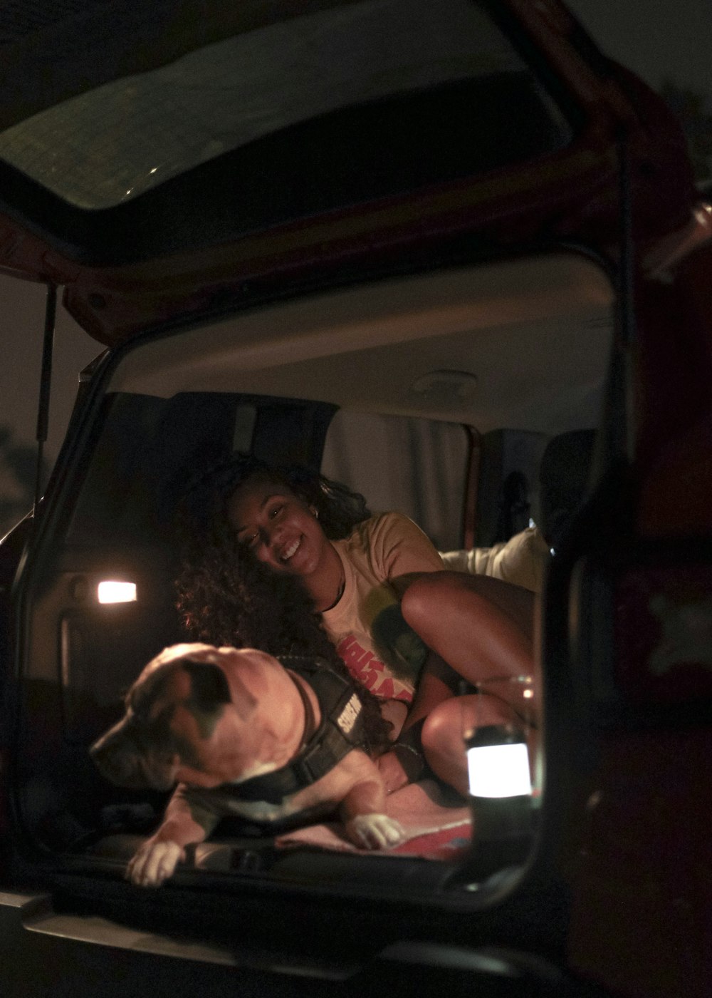 woman in black tank top sitting on car seat beside white and brown short coated dog