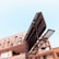A large urban billboard stands in front of a modern multi-story building with numerous windows. The clear sky provides a stark contrast to the dark structure of the billboard, which is devoid of any advertising material.