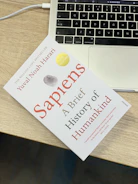 A cinematic shot of the book 'Human Evolution in the Age of AI' beside a glowing laptop.