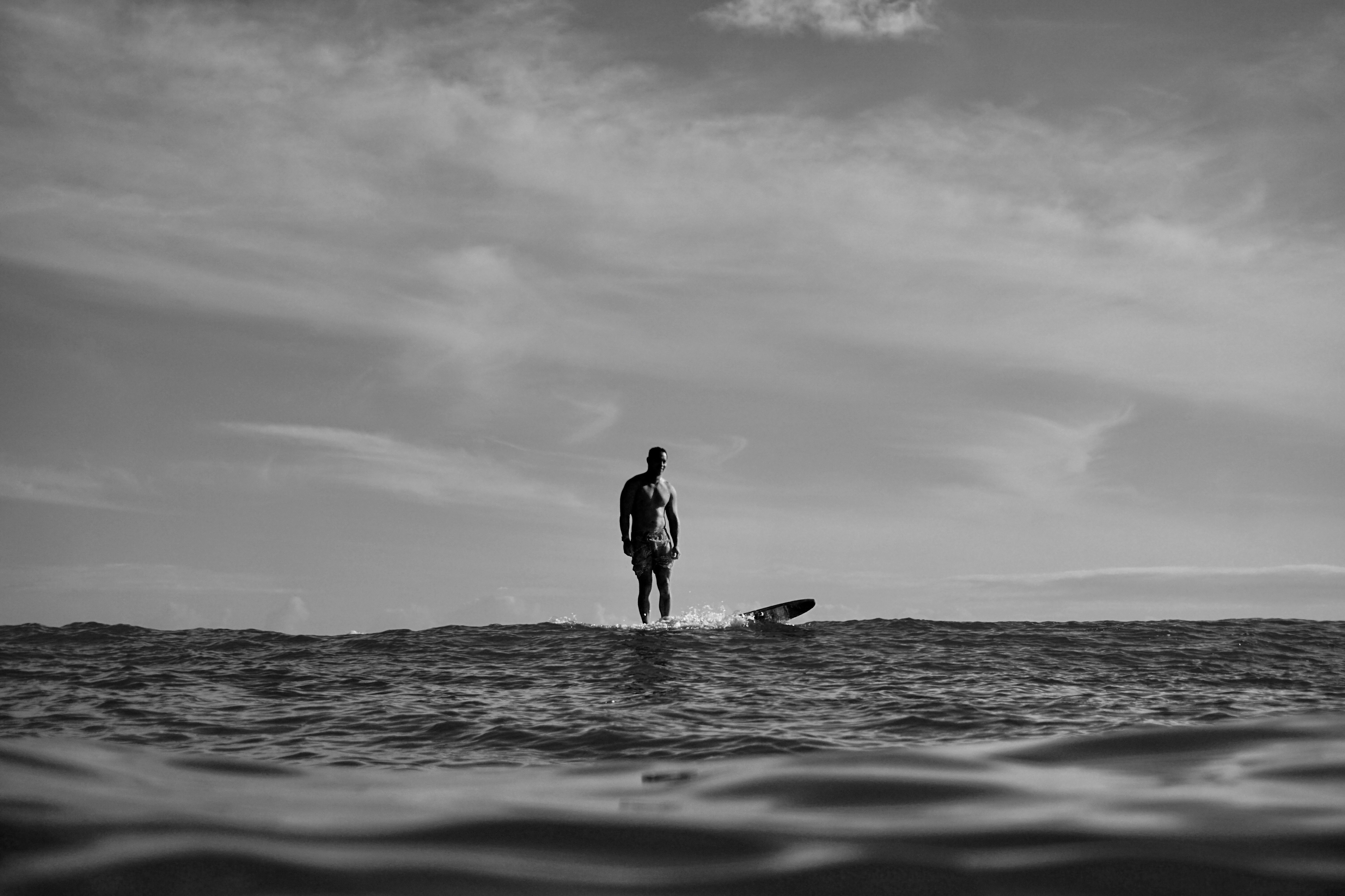 silhouette of man standing on surfboard in the middle of the sea