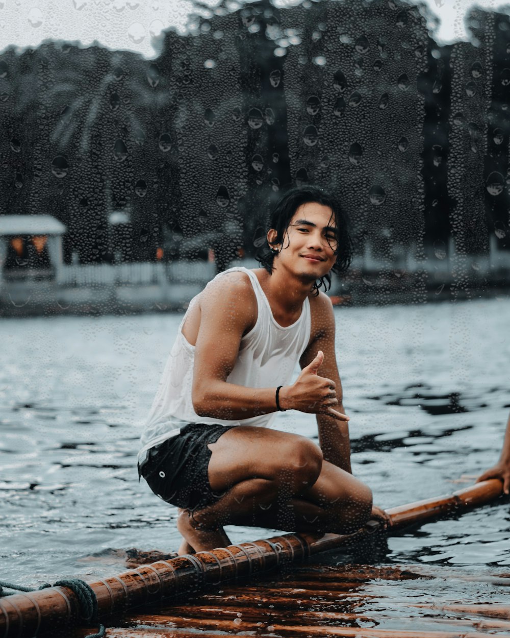 man in white tank top sitting on brown wooden log on water during daytime