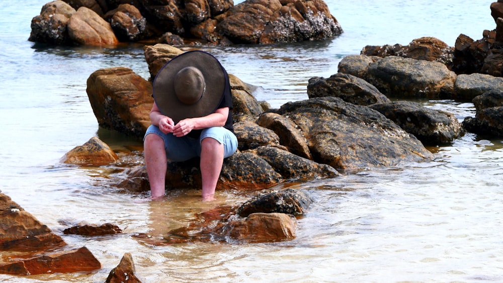 woman in pink shirt sitting on rock in the sea