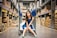 Photo of a smiling woman packing boxes in a bright warehouse with blue and orange accents.