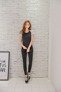 A woman wearing a chic black cotton t-shirt with minimalist accessories, standing against a neutral-toned wall.