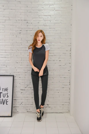 A young woman wearing a black t-shirt with a romantic Italian phrase, standing against a minimalist white wall.