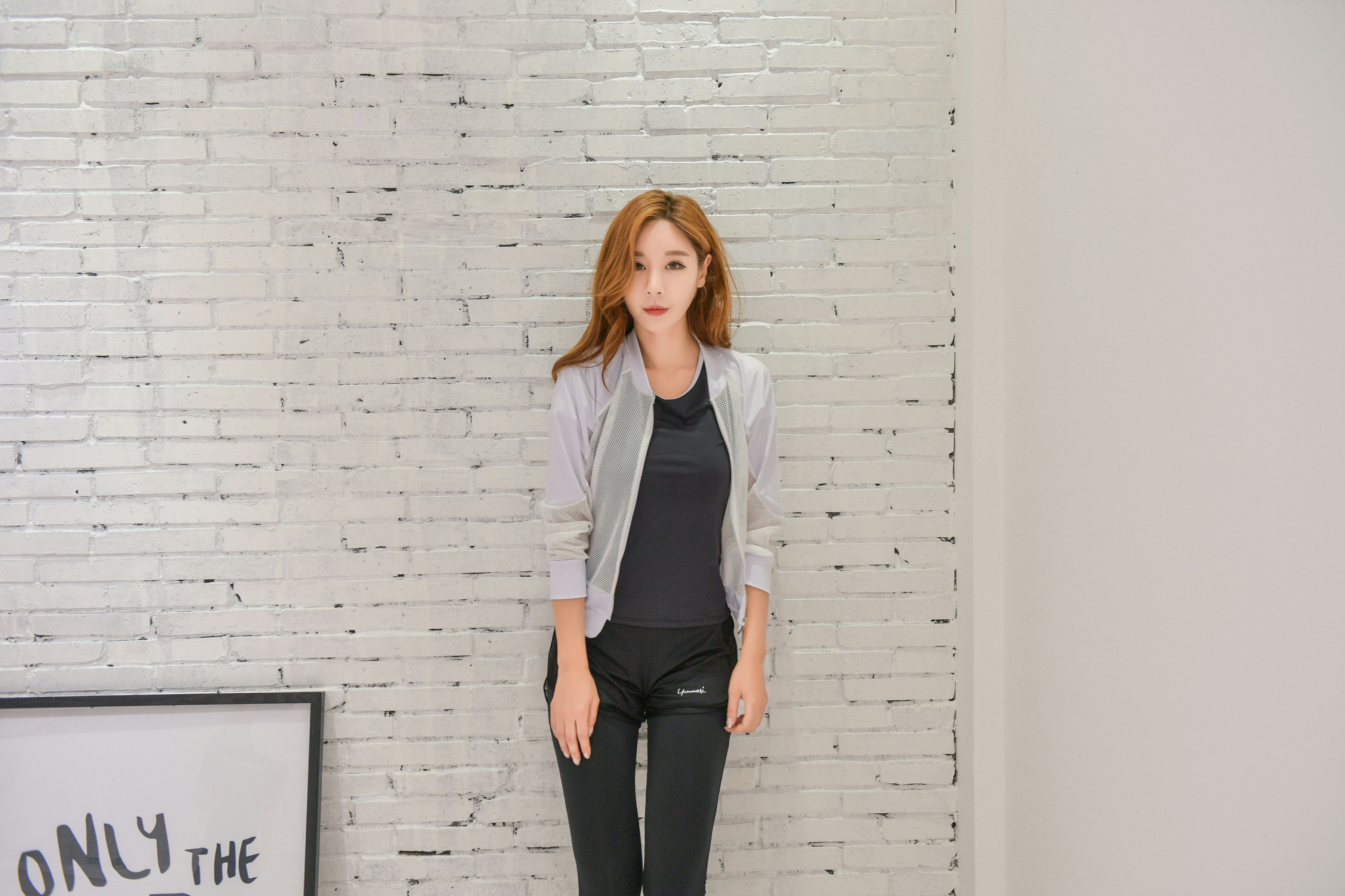 woman in white long sleeve shirt and black pants standing beside white wall