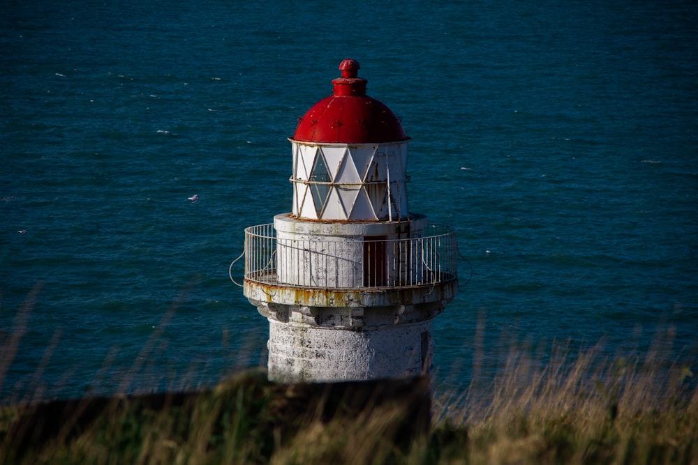 Weißer und roter Leuchtturm auf grünem Grasfeld neben blauem Meer tagsüber