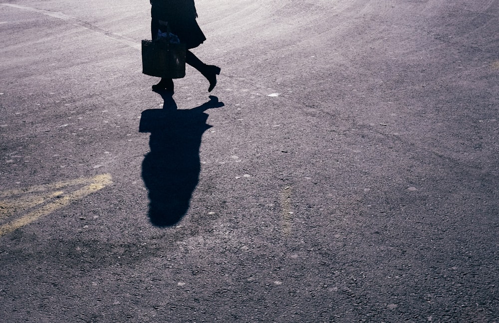 person in black coat walking on gray asphalt road during daytime