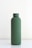 A matte dark green cylindrical bottle with a screw-on cap is placed on a smooth, white surface against a plain background. The design is minimalistic and modern, emphasizing simplicity.