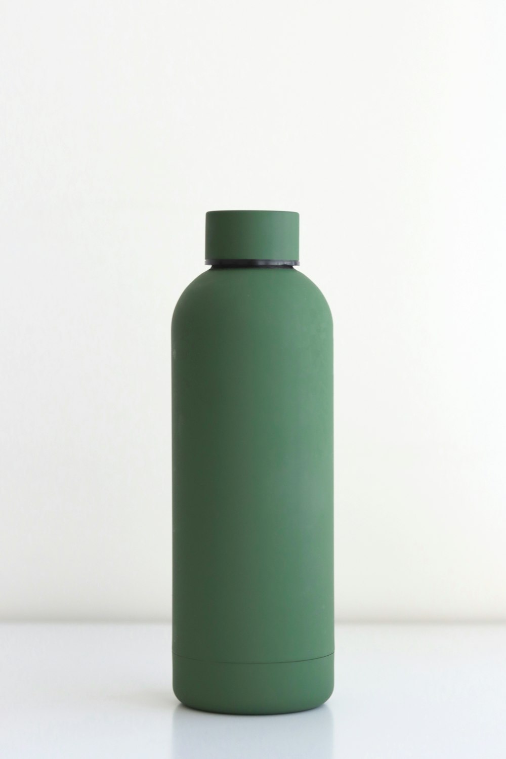 botella verde sobre mesa blanca