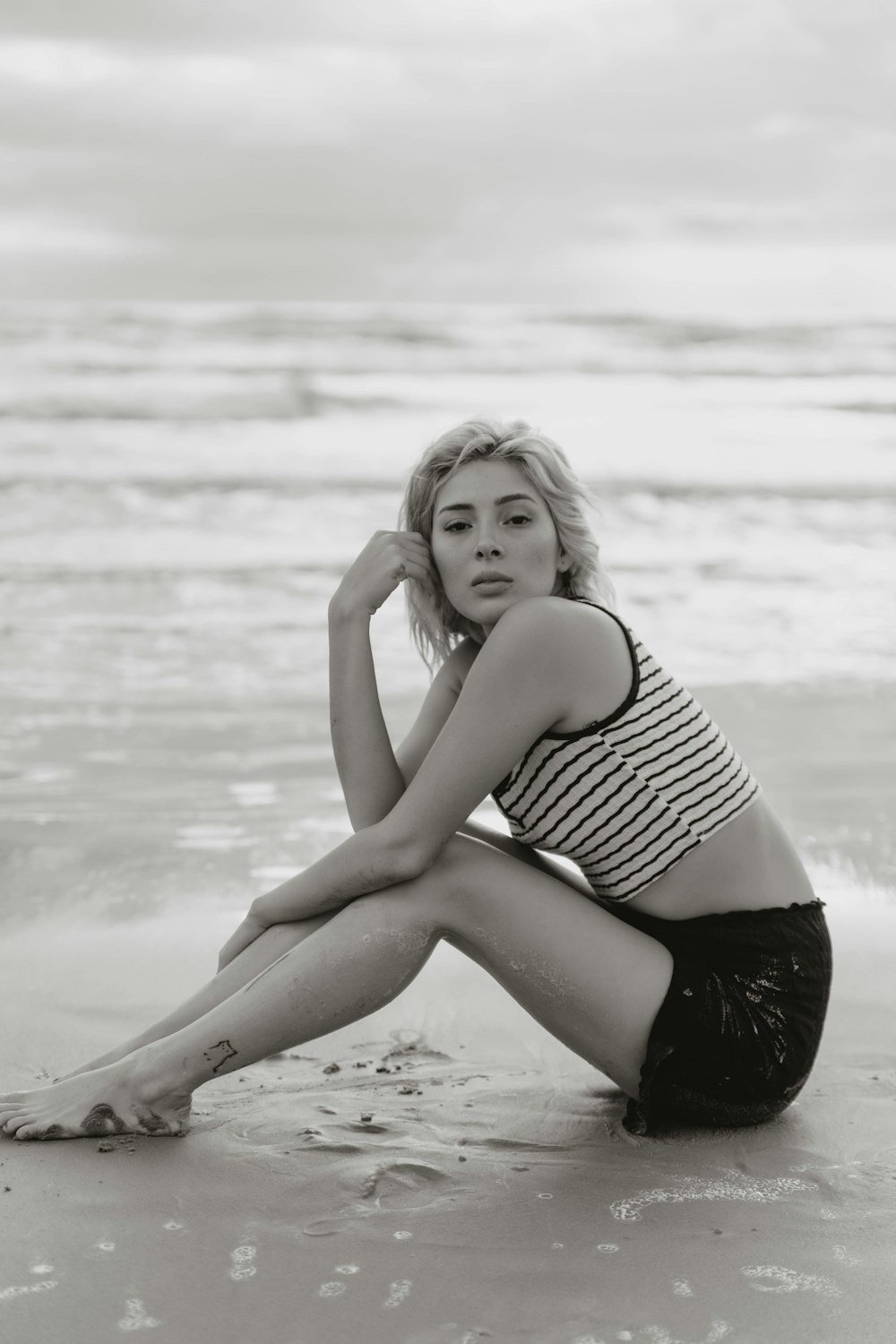 woman in black and white stripe tank top sitting on beach shore