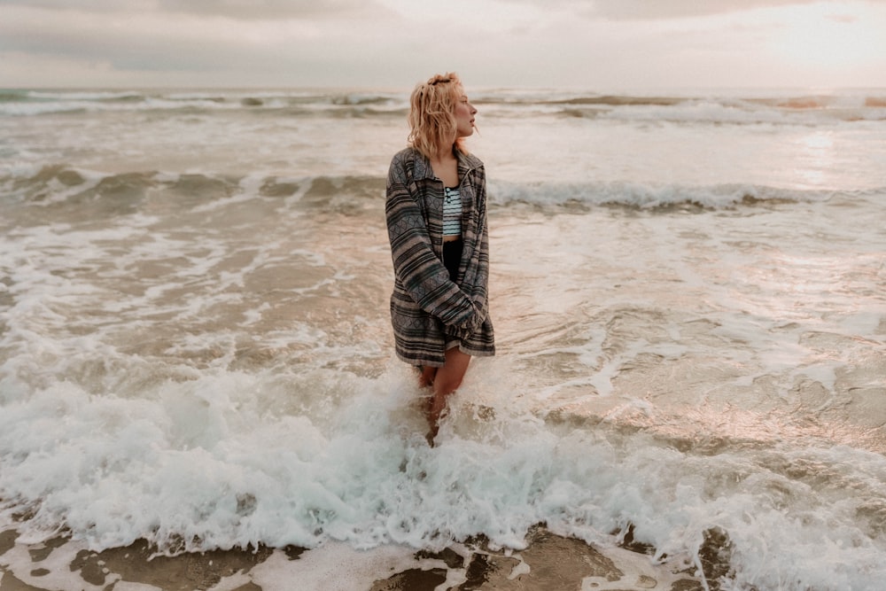 femme en chemise à manches longues noire et blanche debout sur le bord de la mer pendant la journée