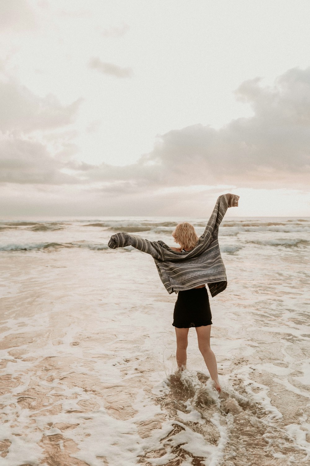 woman in gray long sleeve shirt and black skirt standing on beach during daytime