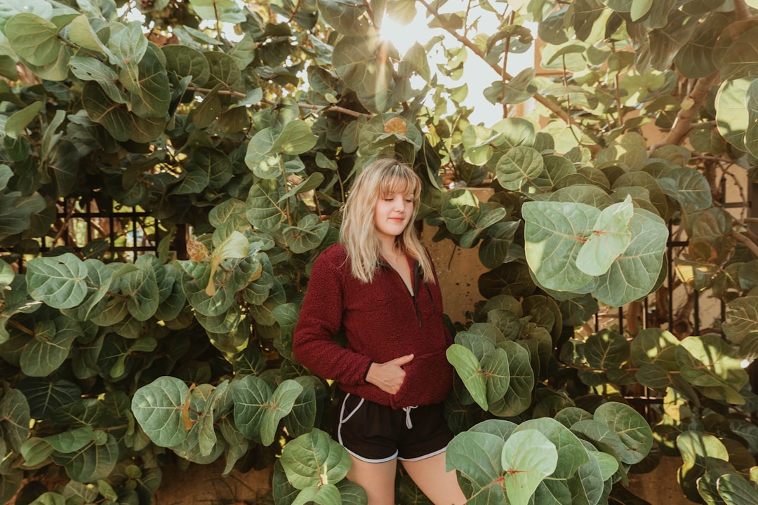 woman in red long sleeve shirt standing beside green plant