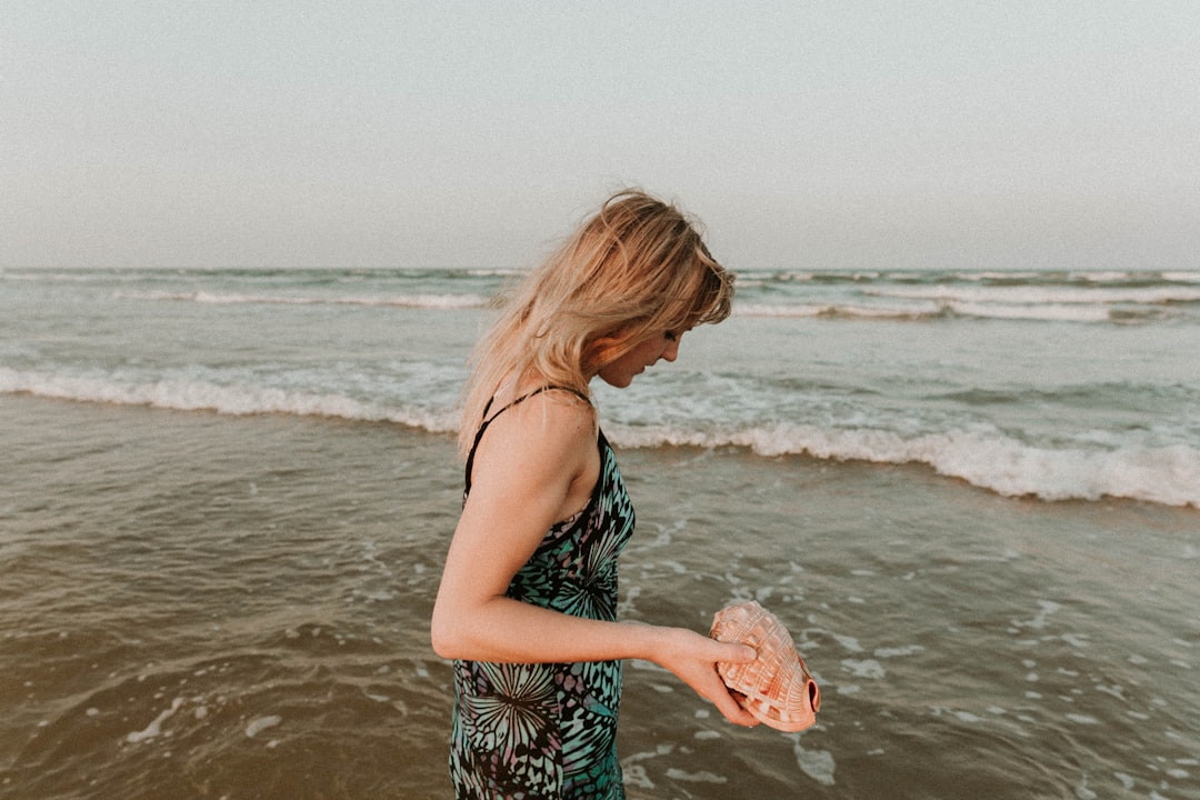 woman in black and white floral spaghetti strap dress standing on beach during daytime