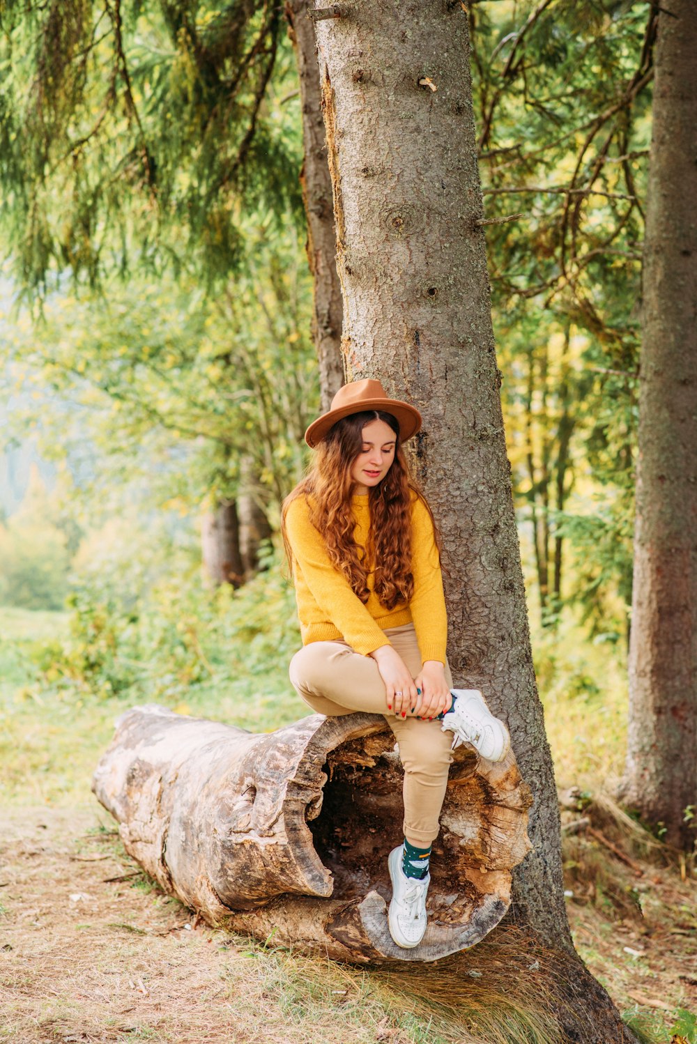 woman in yellow long sleeve shirt and white pants sitting on brown tree log during daytime