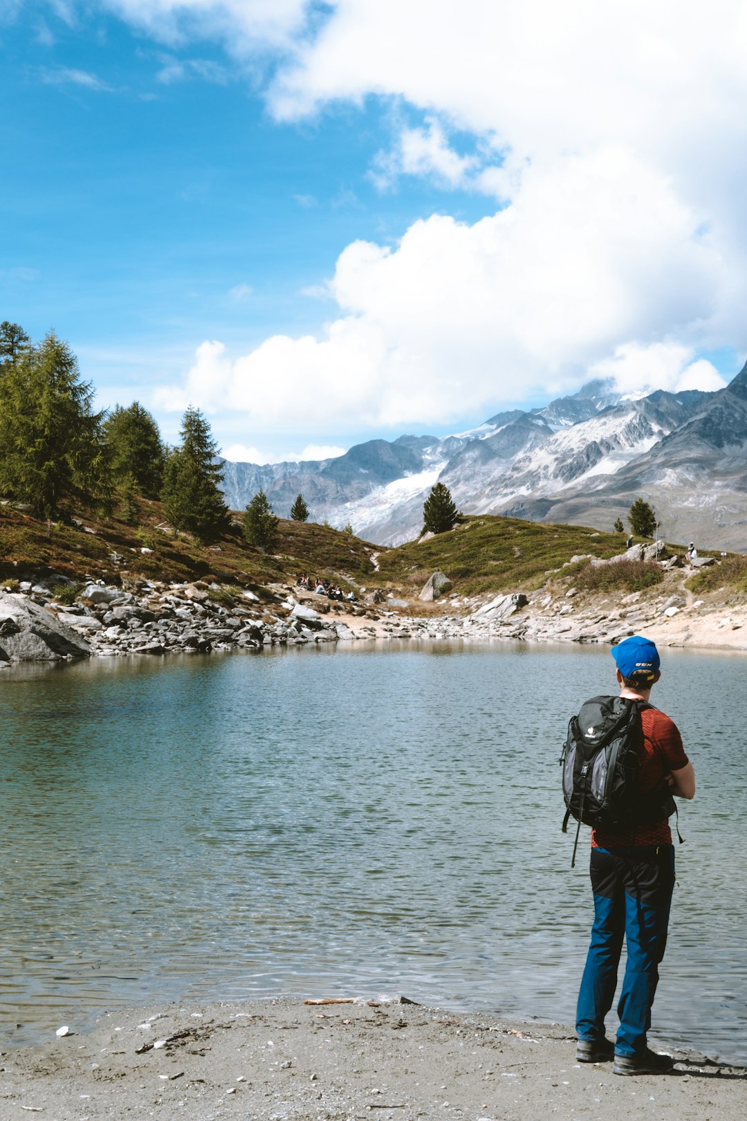 man in blue jacket and black backpack standing on rock near body of water during daytime