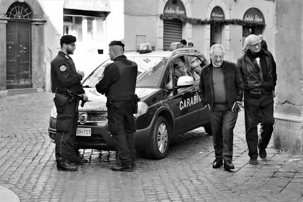 grayscale photo of man in police uniform standing beside car