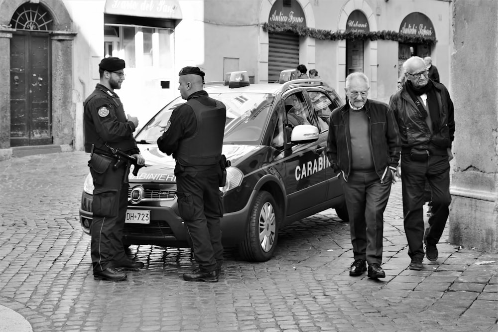 grayscale photo of man in police uniform standing beside car