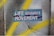 A textured wall with cracks features a prominent sticker displaying the words 'Life Requires Movement' in bold, white letters. The background is a mix of gray and yellow spray paint, creating a dynamic, urban feel.